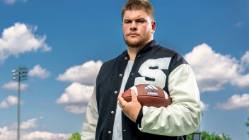Cousins in letterman jacket holding football on the field, photo by Cardoni